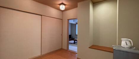 Un pasillo con puertas correderas, suelo de madera y una zona de kitchenette con refrigerador y hervidor.