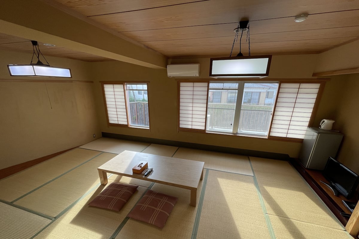 A tatami mat room with a low table, cushions, sliding shoji doors, and a TV on a stand.