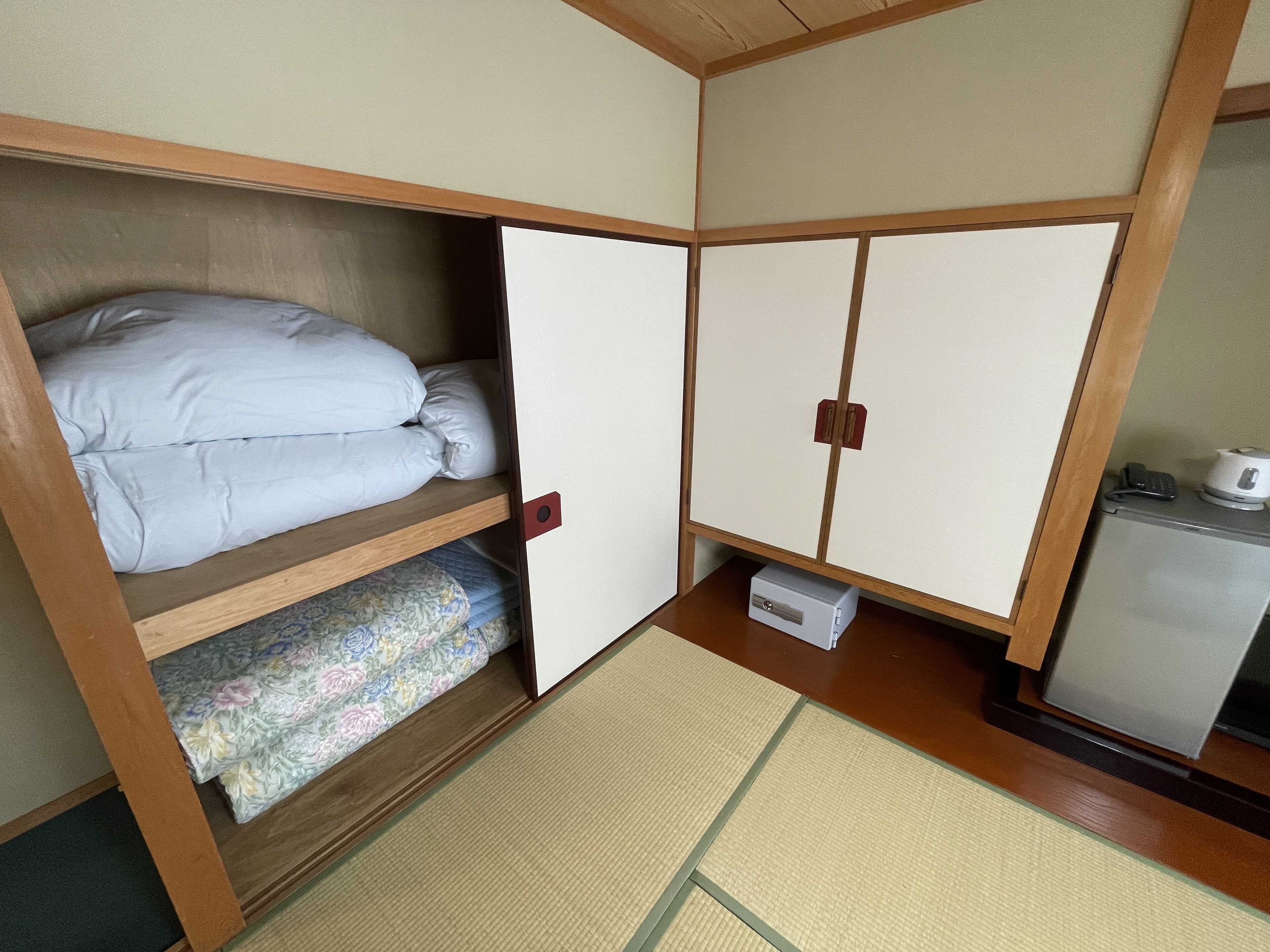 Habitació petita amb un llit superposat, una cuineta compacta i un terra de mats de tatami.