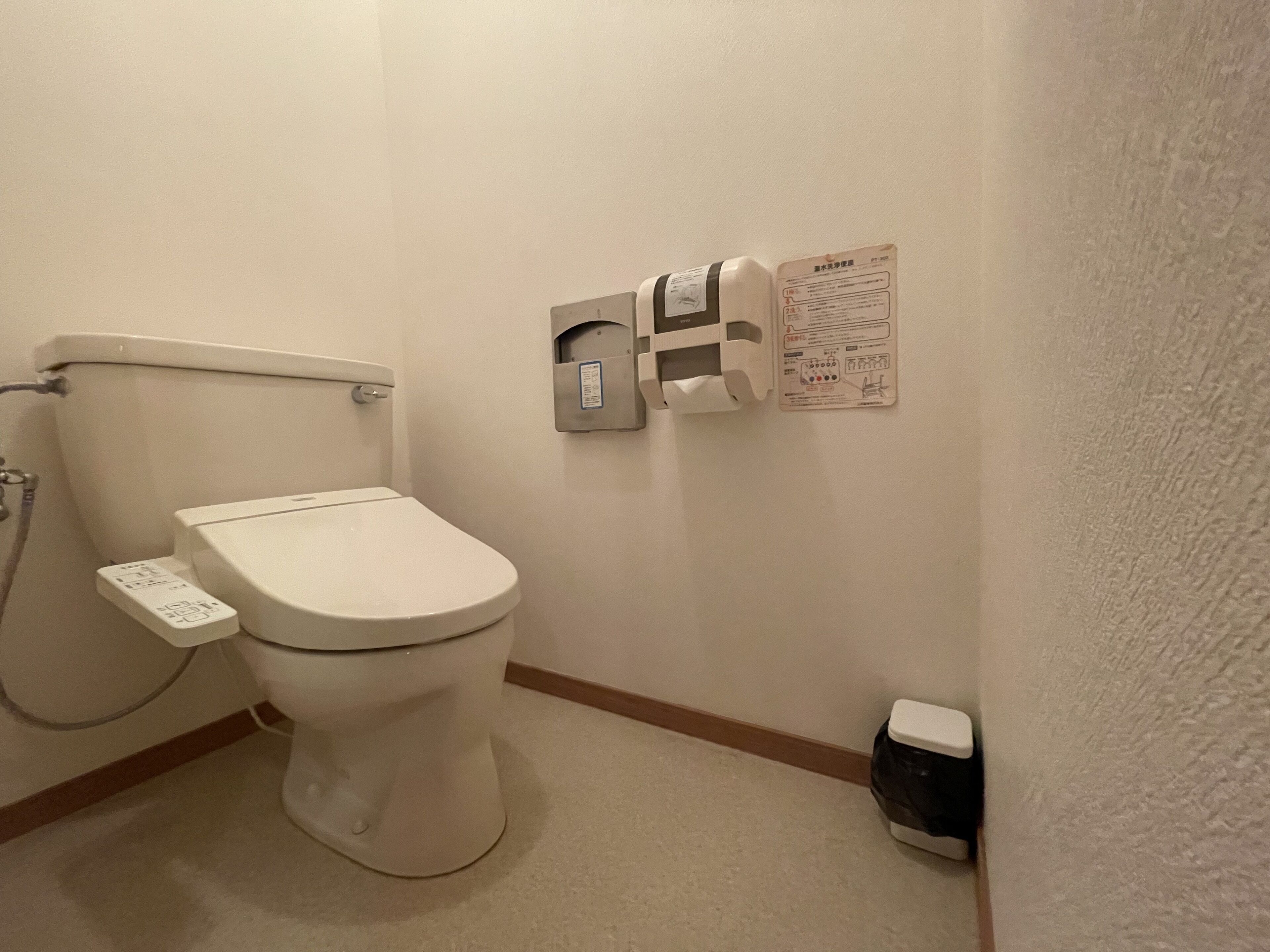 Des toilettes blanches classiques, équipées d’un siège-bidet, d’un sèche-mains et d’un distributeur de papier fixé au mur.