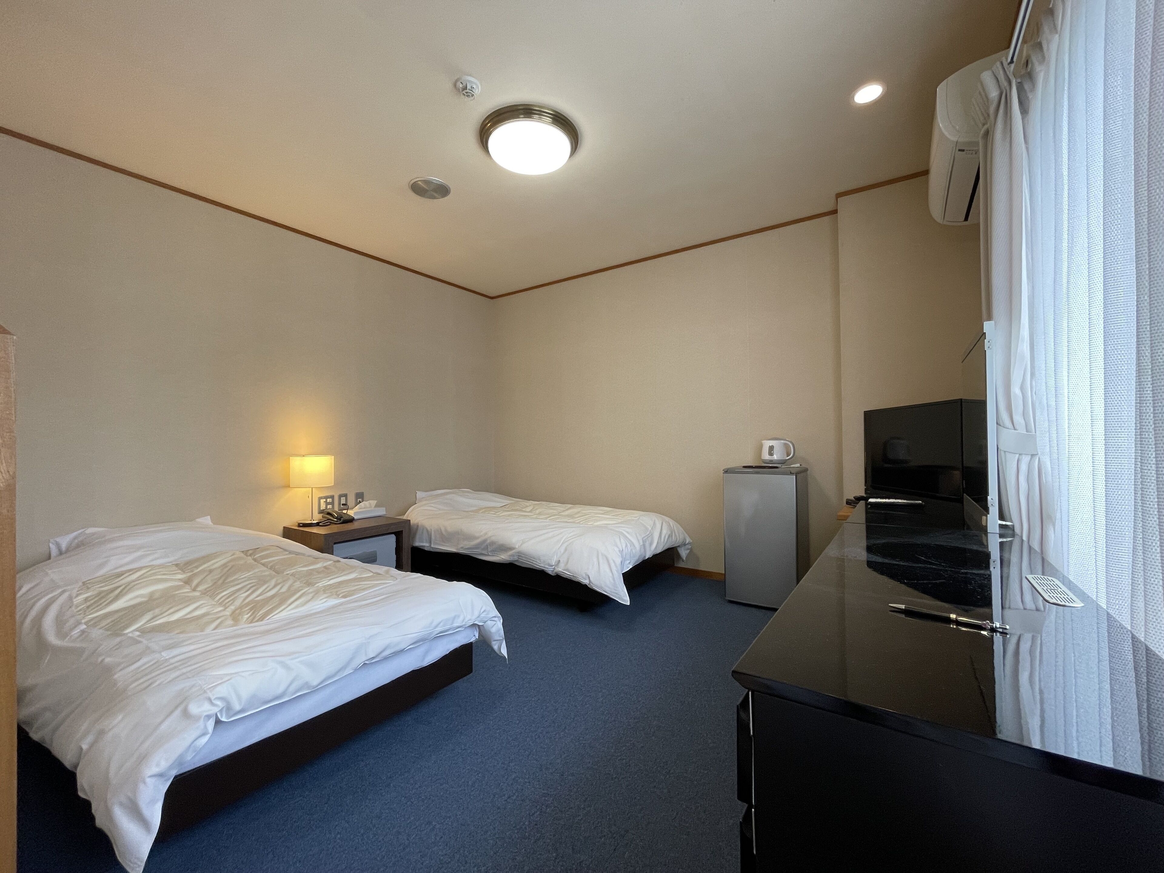 Une chambre d’hôtel avec deux lits simples, un bureau avec un ordinateur, un petit réfrigérateur et une télévision.