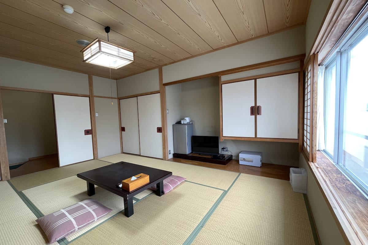 A traditional Japanese room with tatami flooring, a low table, sliding doors, and a TV.