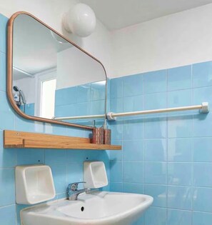 Un baño con lavamanos, espejo, toallero y paredes con azulejos azules.