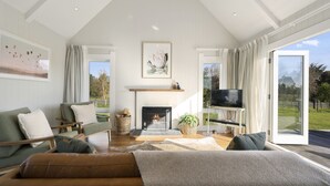 A spacious living room with a fireplace, a television on a stand, and a large window offering a view of the outdoors.
