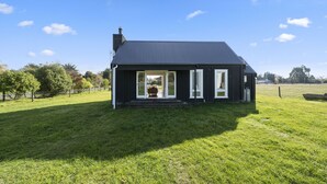 A black house with a sloped roof, a chimney, and a large sliding glass door leading to an outdoor seating area.