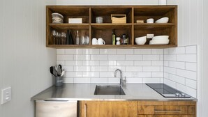 A kitchen with a wooden upper shelf holding glassware, a stainless steel sink, and a dishwasher.