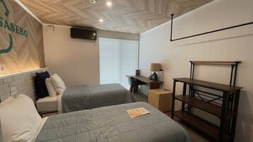 A hotel room with two beds, a desk, a chair, a lamp, and a bench.