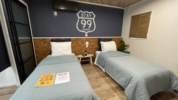 Habitació d'hotel amb dos llits, un panell de fusta al capçal, un televisor fixat a la paret i un cartell de 'Stay 99 Sasebo'.