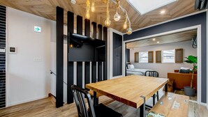 Ein modernes Interieur mit einem Holzesstisch, schwarzen Stühlen, einer schwarzen Akzentwand und einer Decke mit freiliegenden Balken und hängenden Lampen.