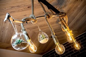 A ceiling with exposed wooden beams and a rustic rope chandelier with clear glass bulbs containing plants.