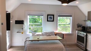 A bedroom with a bed, a desk, two windows, a ceiling fan, and a kitchen area with a stove. - New Remodeled Studio in Oakland's Dimond District (Oakland)