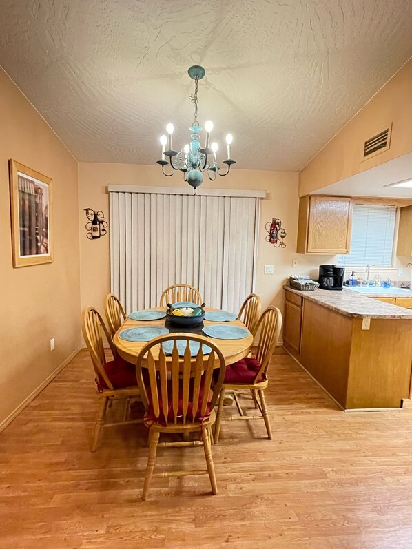Un comedor con una mesa redonda, sillas de madera, una araña y una zona de cocina con encimera y armarios.