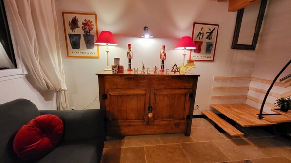 Een woonkamer met een donkergrijze bank, een rode kussen, een houten kast met decoratieve objecten, en twee rode lampen.