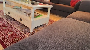 A cozy living room with a wooden ceiling, a sofa with red cushions, a glass coffee table with books and decorative items, and a red patterned rug. - 5km from the town center! Cosy villa in a haven of peace (Uzès)