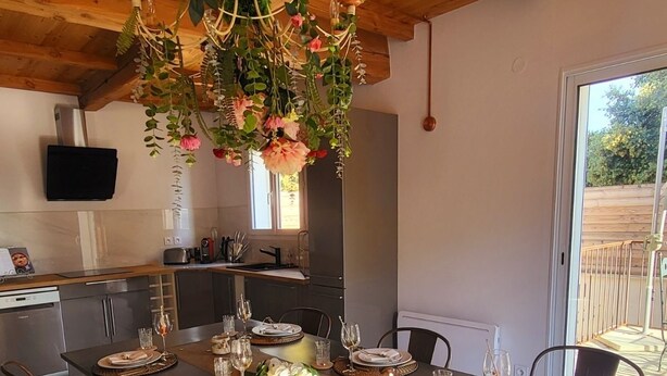 A dining area with a long table set for six, surrounded by wooden chairs. A chandelier with floral decorations hangs above. - 5km from the town center! Cosy villa in a haven of peace (Uzès)