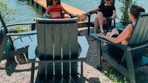 A lakeside patio with outdoor seating under a large umbrella, overlooking boats on the water. - Private Lakefront Beach House off Naramata Bench with sauna and hot tub (Penticton)