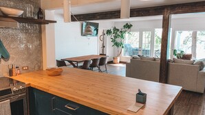 A modern kitchen with a wooden island, black cabinets, and a dining area with a table and chairs. - Private Lakefront Beach House off Naramata Bench with sauna and hot tub (Penticton)