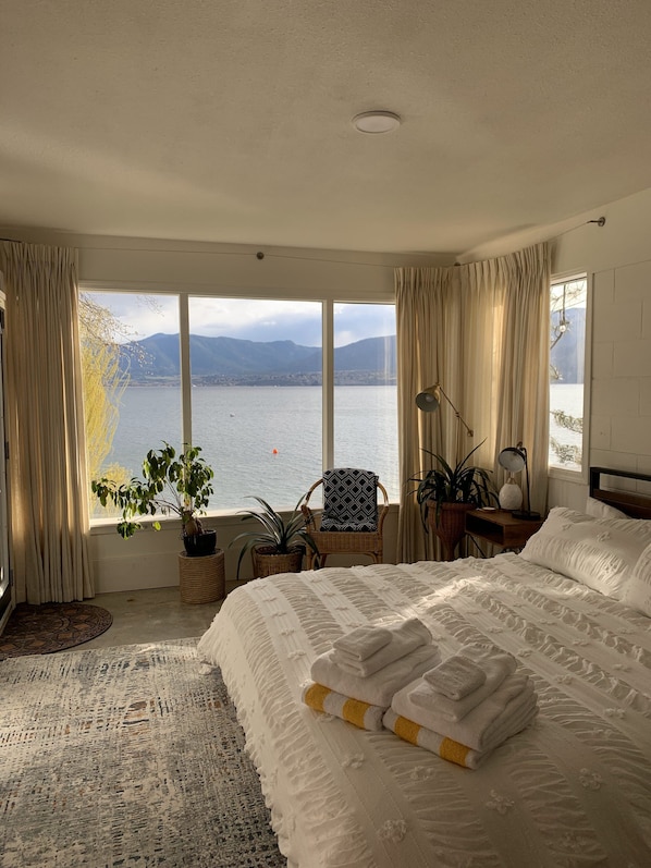 A hotel room with a large bed, a view of a lake, and several potted plants.