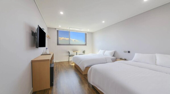 A hotel room with two beds, a TV, a desk, and a window with a view of the sky. - Aroomi Hotel Hyupjae (Jeju City)