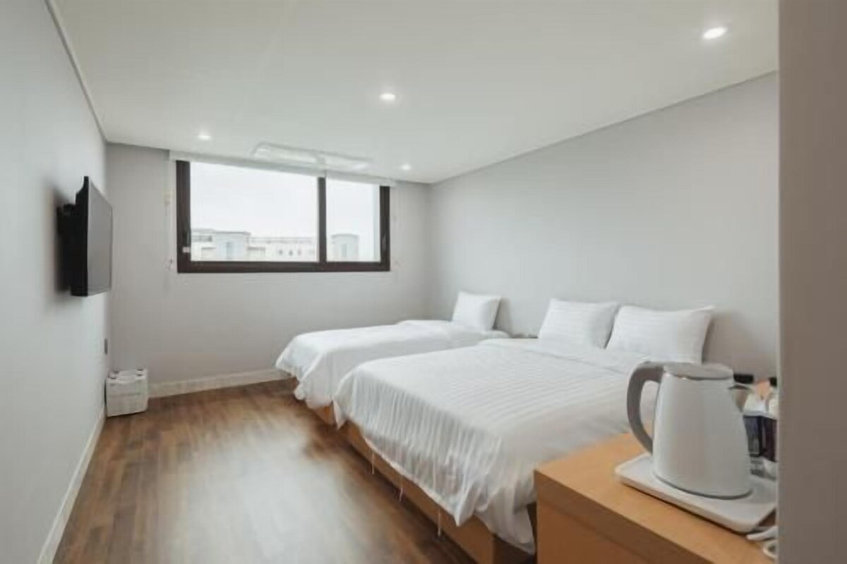 Habitación de hotel con dos camas, piso de madera, ventana con vistas a la ciudad y una cafetera en la mesita de noche.