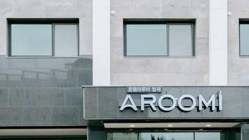 A building with a sign for 'AROOMI' and a window with a reflection of trees.