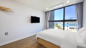 Habitación de hotel con cama, televisor montado en la pared, ventana con cortinas y piso de madera.