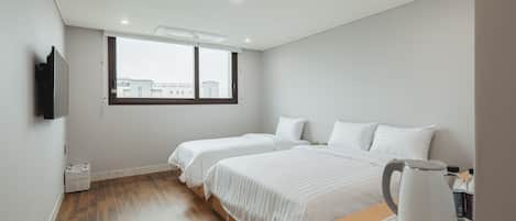 Une chambre d’hôtel avec deux lits, un plancher en bois, une fenêtre, un téléviseur à écran plat et une bouilloire posée sur une table.