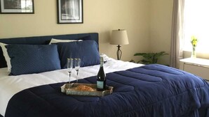 A neatly made bed with a dark blue comforter, a tray with a bottle and glasses, and a small plant by the window. - Desert Falls Country Club (Palm Desert)