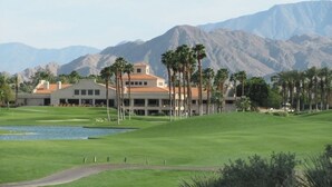 A golf course with a clubhouse, palm trees, and mountains in the background. - Desert Falls Country Club (Palm Desert)