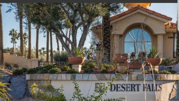 A pool area with a sign reading "DESERT FALLS" and a building with a tiled facade and arched windows. - Desert Falls Country Club (Palm Desert)