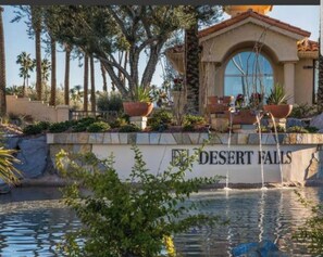 Uma área de piscina com uma placa que diz "DESERT FALLS" e um edifício com fachada de azulejos e janelas em arco.