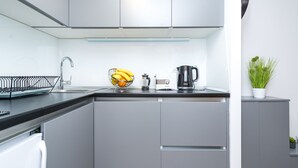 A modern kitchen with grey cabinets, a black countertop, a sink, a kettle, and a bowl of bananas. - Apartment Kantun (Dubrovnik)