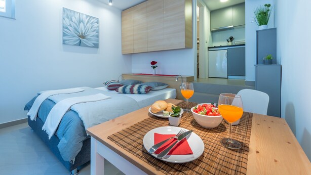 A modern bedroom with a bed, bedside table, and a view of the kitchen. - Apartment Kantun (Dubrovnik)