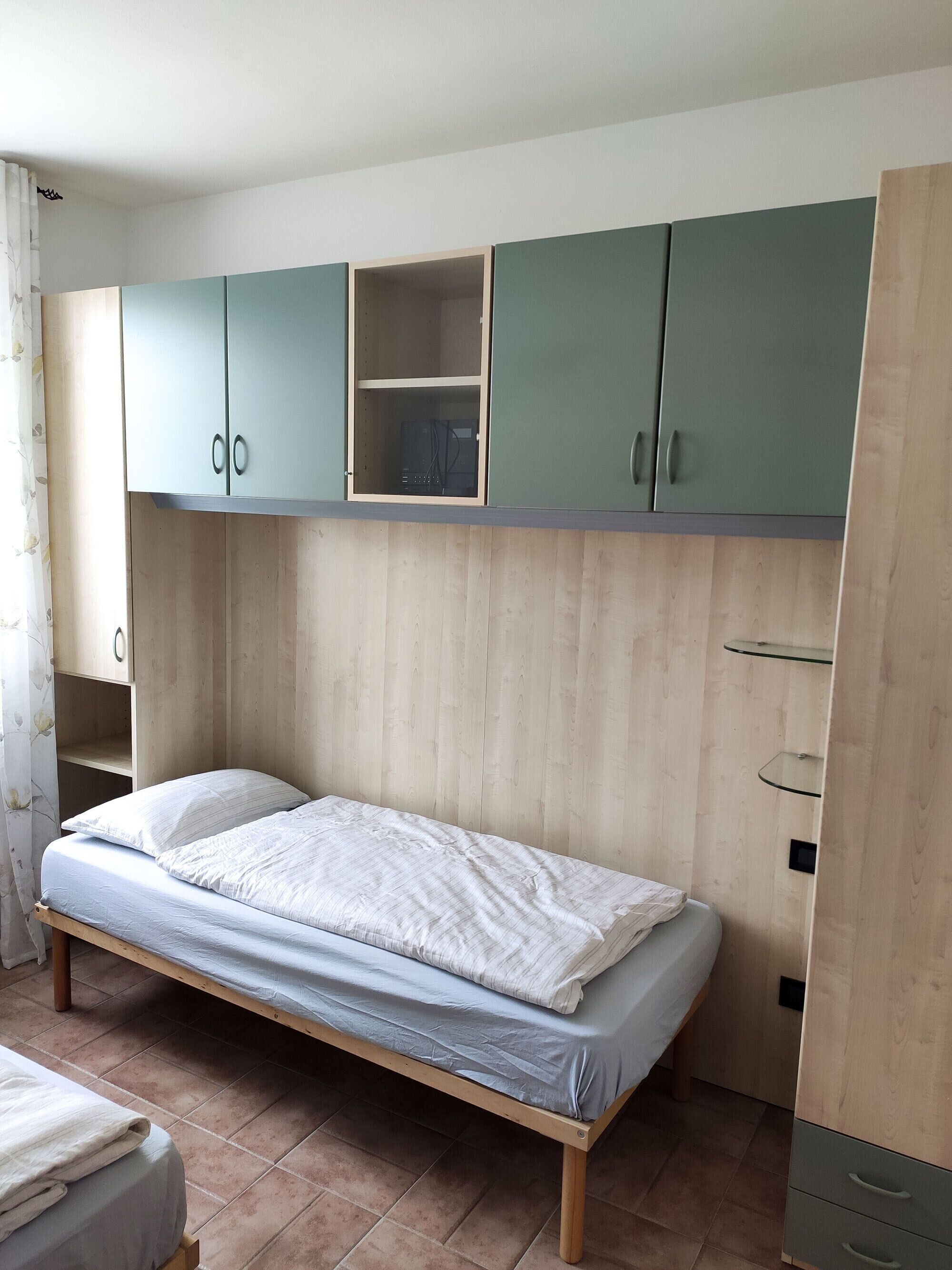 A bedroom with a bed, wooden wardrobe, and a small shelf unit.