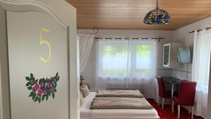 Ett rum med en säng, ett skrivbord med en stol, en tv och ett fönster med gardiner.