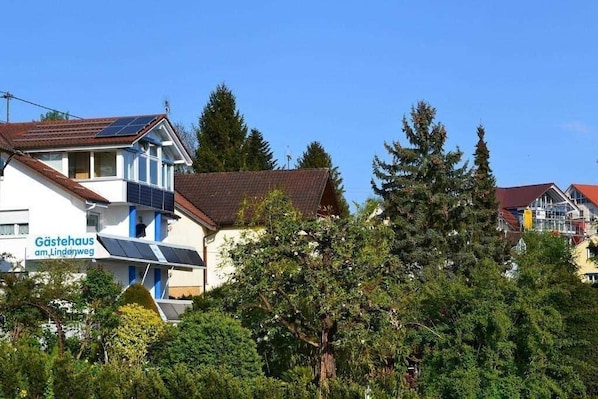 A building with solar panels, a sign reading 'Gästehaus am Lindenweg,' surrounded by trees.