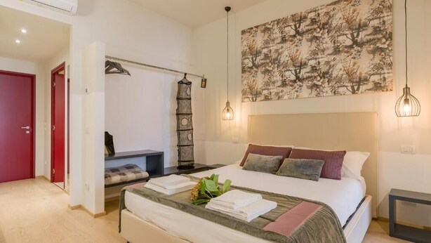 A bedroom with a bed, a wall-mounted artwork, a hanging light fixture, and a bedside table. - Velluto Blu (Verona)