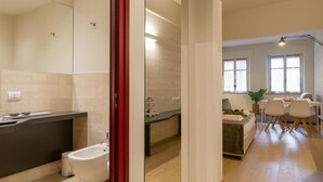 A modern bathroom with a bathtub, a vanity, and a toilet. There is a dining area with a table and chairs visible through an open doorway. - Velluto Blu (Verona)