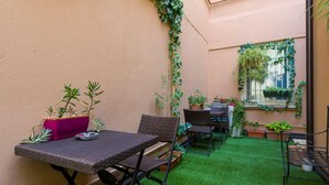 A small patio area with a table and chairs, surrounded by potted plants and a window with greenery. - Velluto Blu (Verona)