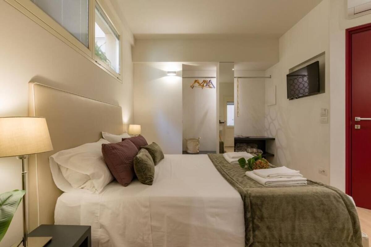 A hotel room with a bed, bedside lamps, a red door, and a small plant.