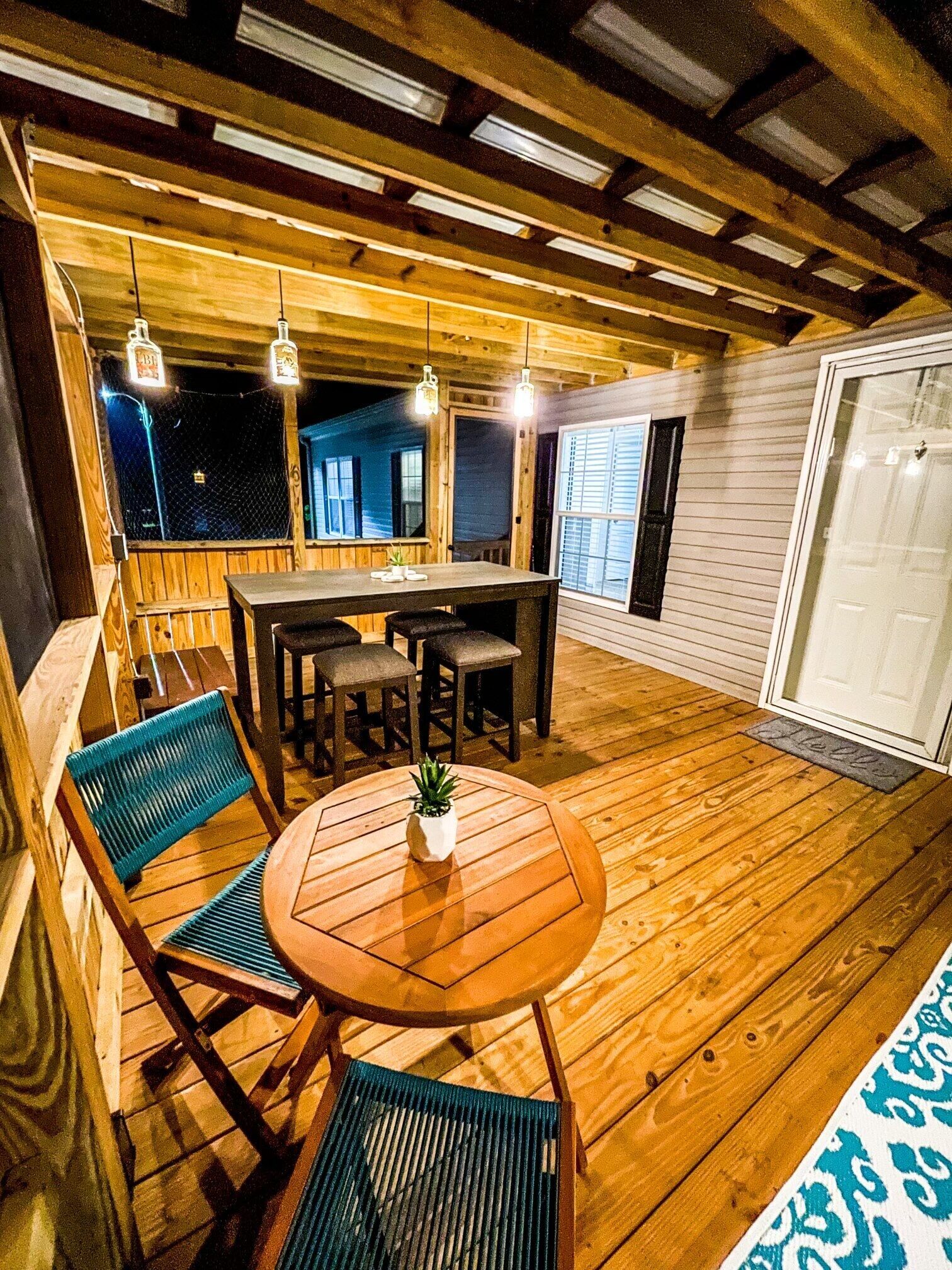 A wooden deck with a round table and chairs, a small potted plant, and hanging lights.
