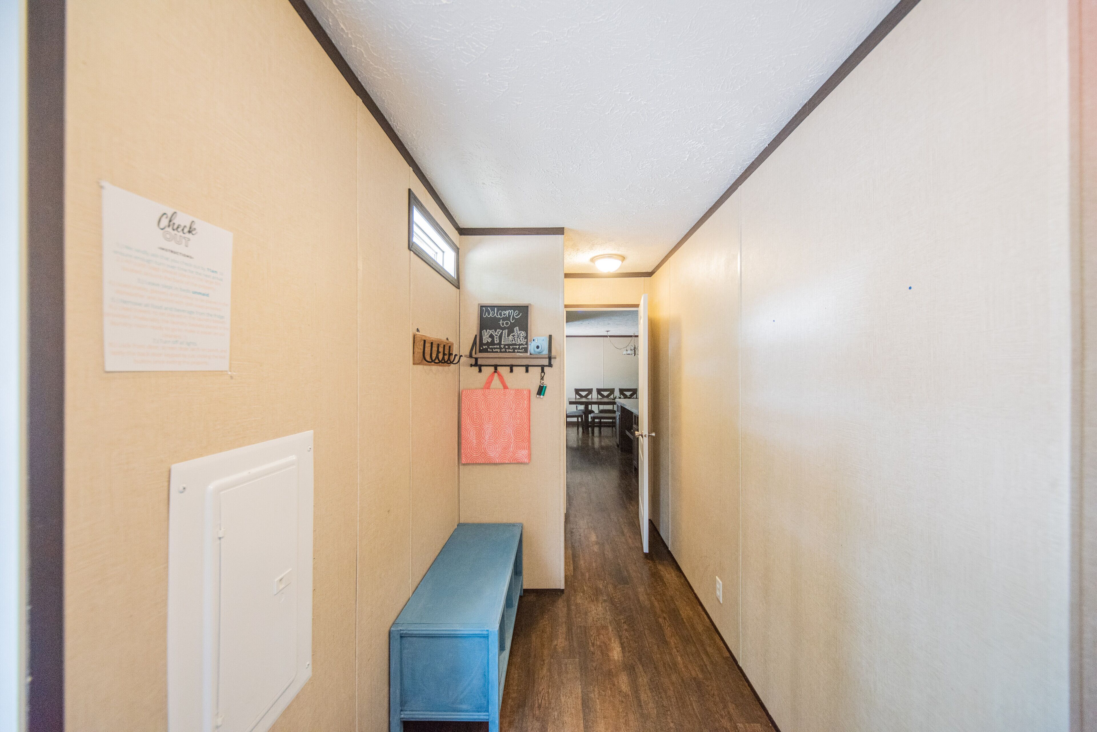 A narrow hallway with a bench, a check-in desk, and a welcome sign.