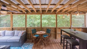 Een overdekt terras met een houten tafel en stoelen, een bank en een bar.