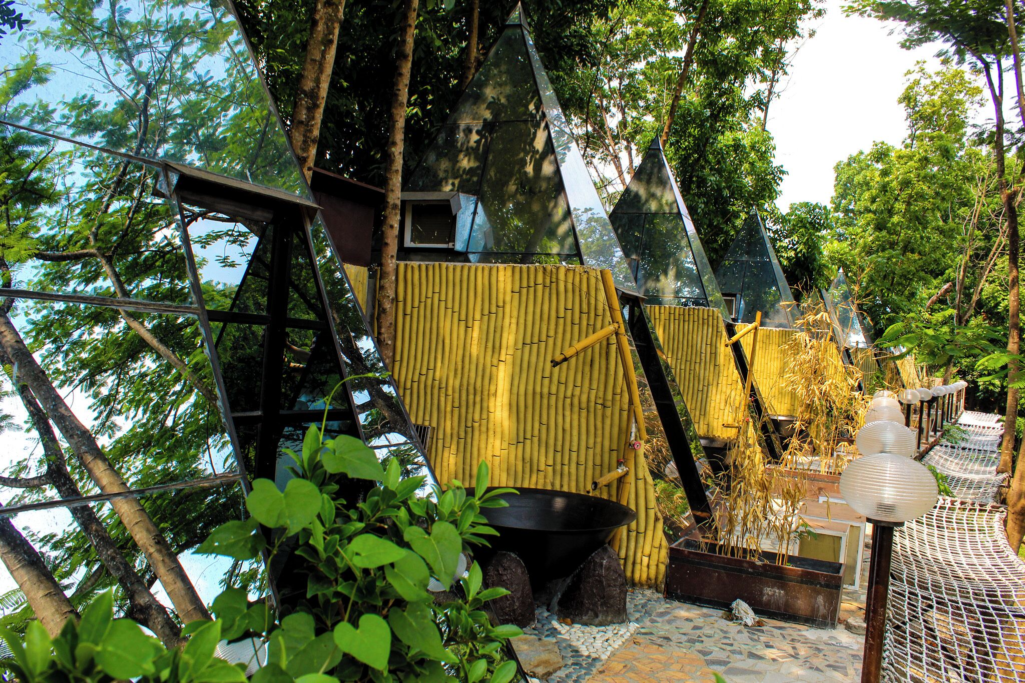Une cabane perchée dans un arbre, avec une structure extérieure en bambou, un lavabo noir et un lampadaire blanc.