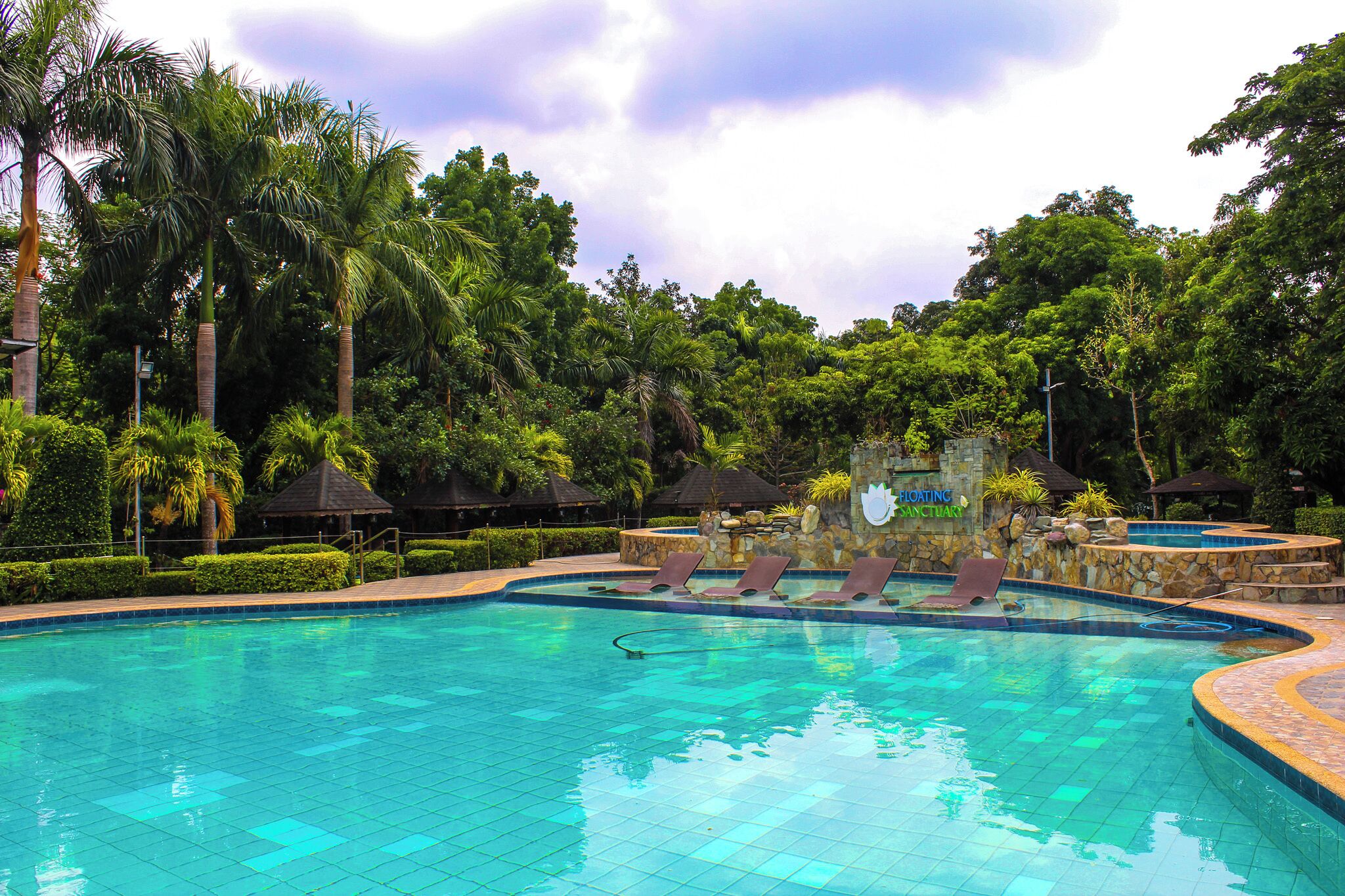 A swimming pool with lounge chairs and a stone wall with a sign reading 'Floating Sanctuary'.