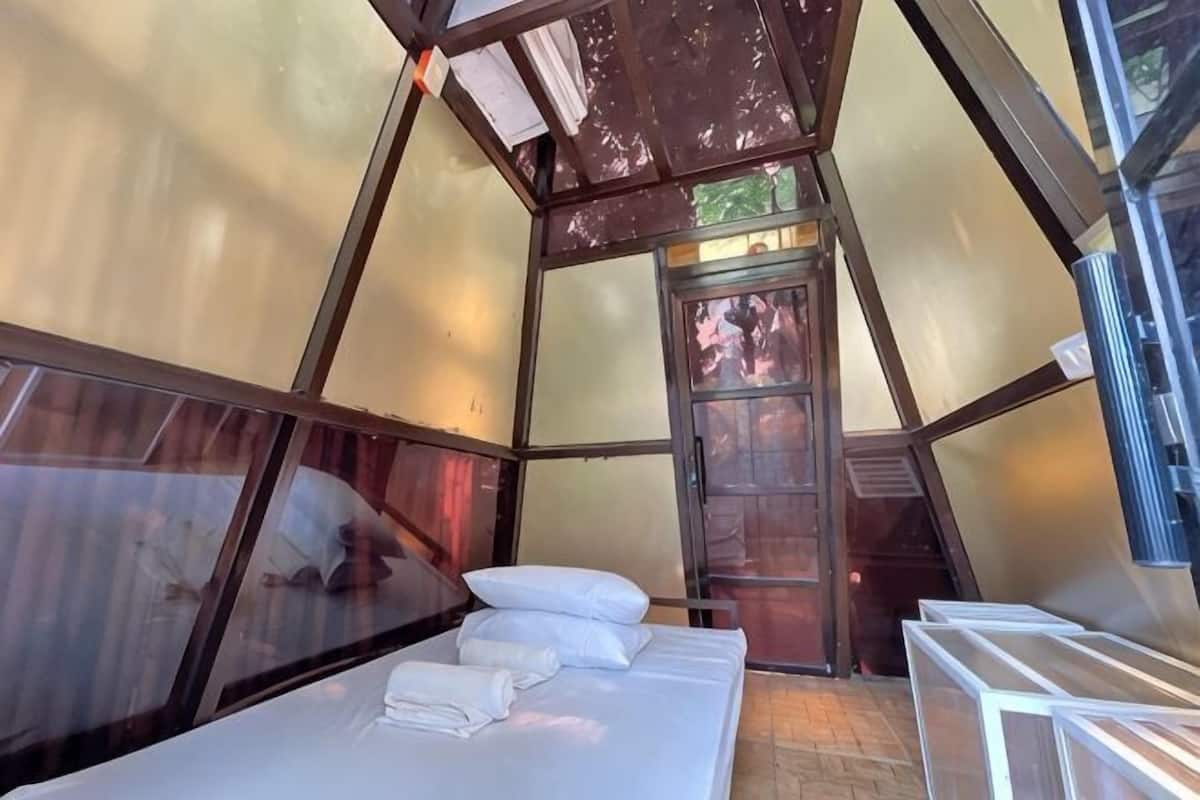 Une pièce triangulaire avec un lit, des oreillers et une fenêtre.