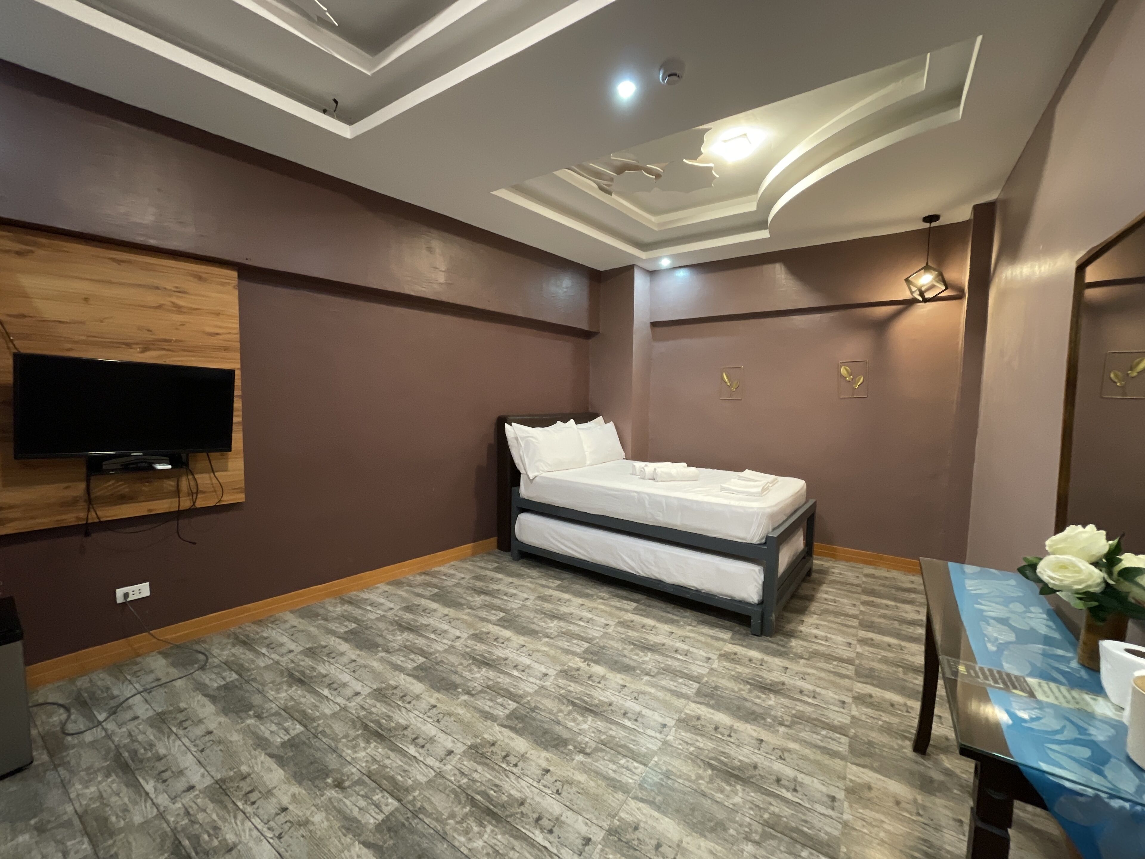 A bedroom with a bed, a TV mounted on the wall, and a table with a vase of flowers.