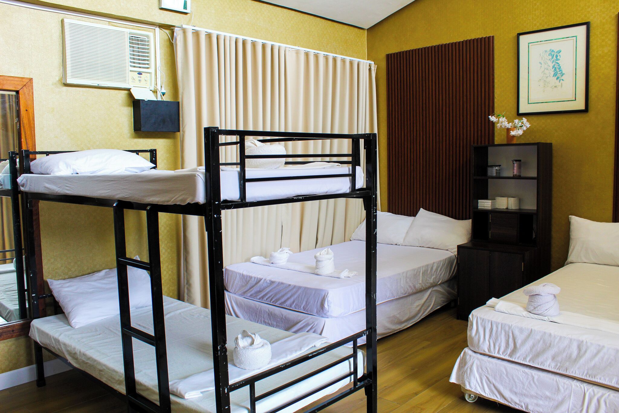 A hotel room with bunk beds, a bedside table with a lamp, a wall-mounted air conditioner, and a framed picture.