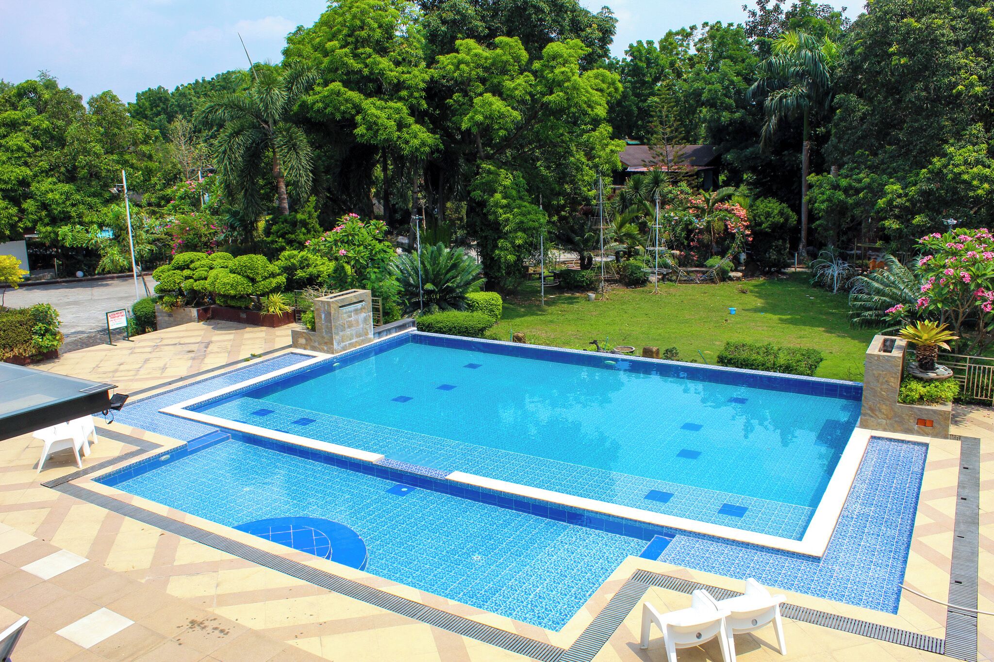 A rectangular swimming pool with a tiled border, surrounded by a paved deck with lounge chairs.