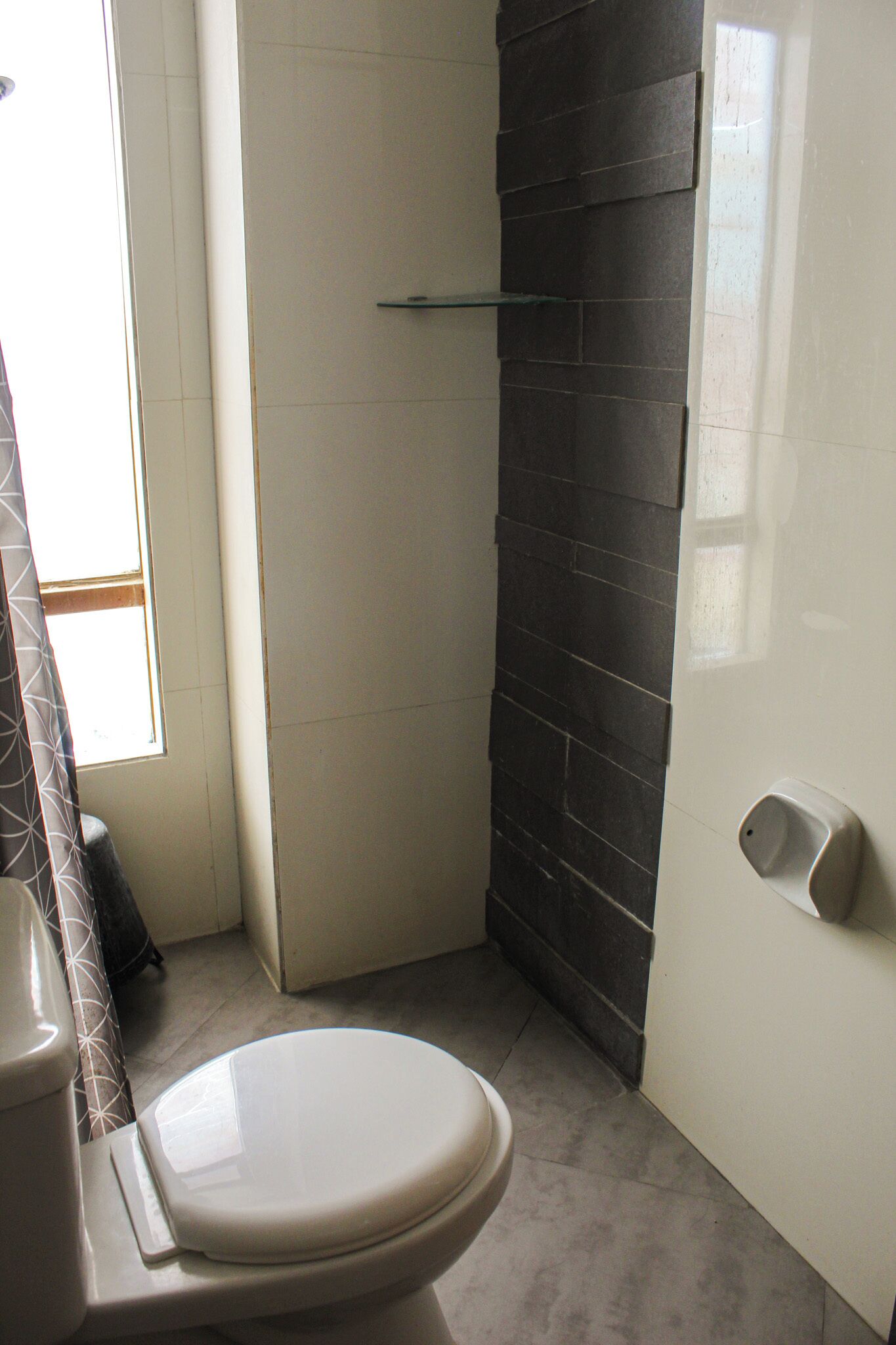 A bathroom with a toilet, a shower area with a glass shelf, and a tiled wall.